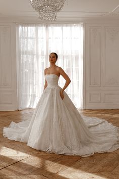 a woman in a white wedding dress standing on a wooden floor next to a chandelier