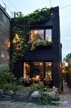 a black house with lots of plants growing on it's side and windows that are lit up