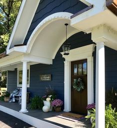 a blue house with white pillars and flowers on the front porch