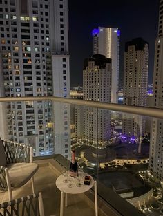 two chairs and a table on a balcony with city lights in the background at night