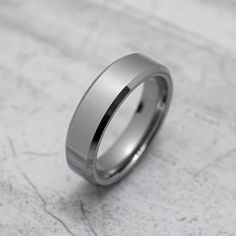 a wedding band is shown on a white marble surface, with the center ring in polished silver