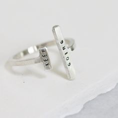 One of our favorite gift-able rings, the Double Adjustable Ring is an eye-catching way to inspire & encourage. An adjustable, asymmetric ring with a tiny phrase of inspiration. Letters are individually stamped by hand, making each ring one of a kind. The message is centered on each bar in our signature teeny-tiny uppercase block font. For an unconventional look, try stacking with our diamond dusted adjustable rings. details+ longer bar measures 5/8" wide x 2 mm tall+ shorter bar measures 1/4" wi Inspirational Adjustable Silver Rings, Modern Personalized Adjustable Stackable Rings, Inspirational Adjustable Sterling Silver Rings, Adjustable Inspirational Sterling Silver Rings, Adjustable Open Ring With Meaningful Style, Inspirational Adjustable Ring, Meaningful Adjustable Open Ring, Adjustable Hand Stamped Midi Rings As Gifts, Meaningful Stackable Sterling Silver Rings For Everyday