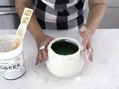 a woman is painting a vase with green paint on the table next to a cup