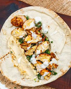 a tortilla with chicken, spinach and white sauce on it sitting on a wooden table