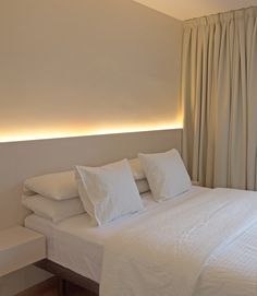 a bed with white sheets and pillows in a bedroom next to a wall mounted light