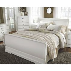 a white bed sitting in a bedroom on top of a wooden floor next to a window