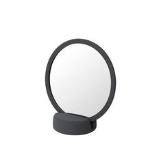 a round mirror sitting on top of a white table next to a black stand with an object in front of it