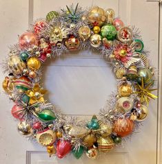 a christmas wreath with ornaments hanging from it's sides on a door frame in front of a white door