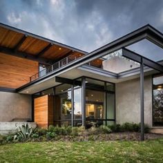 a modern house with glass walls and wood accents on the roof, along with green grass