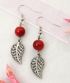 two red beads are hanging from silver earwires on a white surface with pink flowers