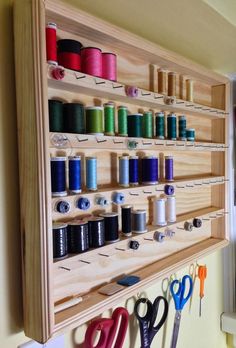 a wall mounted sewing rack filled with spools of thread, scissors and yarn