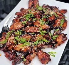 a white plate topped with chicken wings covered in sesame seeds and garnishes