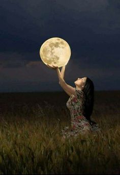 a woman in a field holding up a full moon