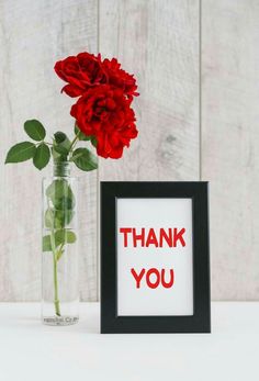 a red rose in a vase next to a framed thank you card with the word'thank you '