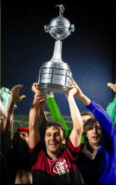 two men holding up a trophy in front of their heads with other people around them