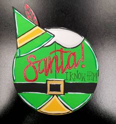 a green and yellow christmas ornament that says santa i know him