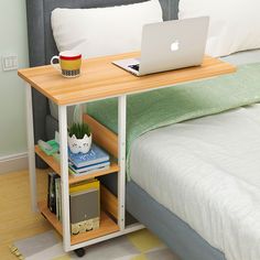 a laptop computer sitting on top of a wooden table next to a bed with white pillows