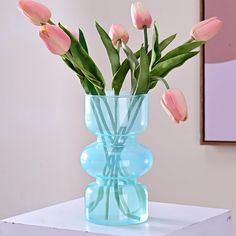 pink tulips are in a blue vase on a white table