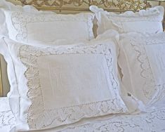 two white embroidered pillows sitting on top of a bed next to a golden headboard