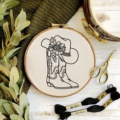 a cross stitch cowboy boot with a flower on it next to some scissors and thread