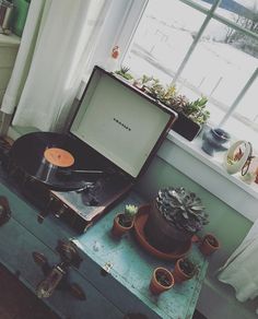 an old record player sitting on top of a suitcase in front of a window with potted plants