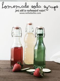 three glass bottles filled with liquid sitting on top of a table next to strawberries