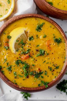 two wooden bowls filled with yellow soup and garnished with parsley