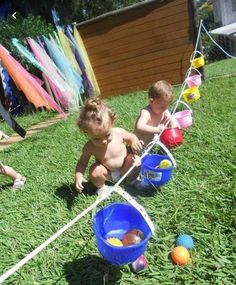 two toddlers playing in the grass with balls and plastic cups on a stick,