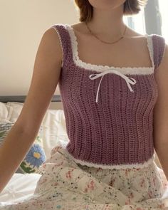 a woman sitting on top of a bed wearing a purple sweater and skirt with white trim