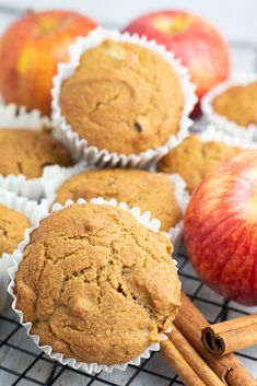 several muffins on a cooling rack with cinnamon sticks and apples in the background