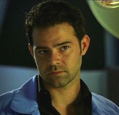 a close up of a person wearing a blue shirt and looking at the camera with an intense look on his face