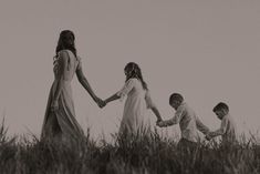 three children holding hands in the grass with their mother and two dads walking behind them