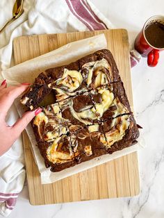 a person is holding onto a brownie on a cutting board next to a cup of coffee