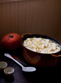 a bowl filled with mashed potatoes next to two small bowls and a pumpkin on the table