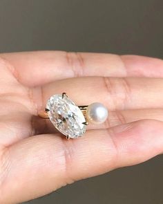 a woman's hand holding an engagement ring with a diamond and pearl on it