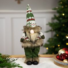 a small stuffed animal wearing a green and white sweater with a christmas tree in the background