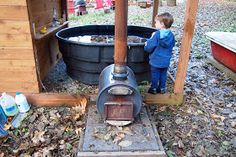 a little boy standing in front of an old fashioned wood burning stove and water tank