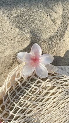 a pink flower sitting on top of a net next to the sand at the beach