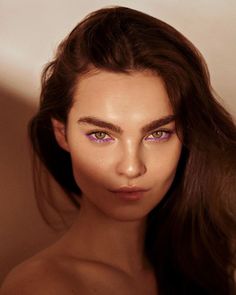 a woman with long brown hair and purple eyeshadow is posing for the camera