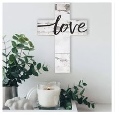 a cross with the word love on it next to a candle and potted plant