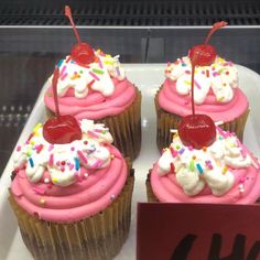 three cupcakes with pink frosting and sprinkles are on display