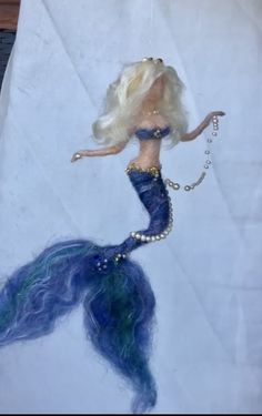 a barbie doll with blue hair and pearls on it's tail, sitting on a piece of paper