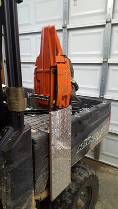 an orange piece of equipment sitting on the back of a forklift in front of a garage door