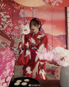 a woman in a red and white kimono sitting on a table with an umbrella over her head