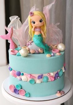 there is a blue cake with a little mermaid on top and pearls around the edges