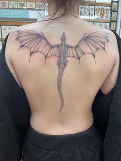 a woman's back with a dragon tattoo on her left shoulder and the wings spread out