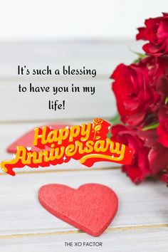 happy anniversary card with red roses and heart on white wooden table next to it's message