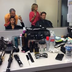 a man is getting his hair cut in front of a mirror while two women look at him