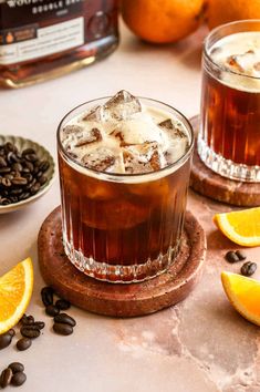 two glasses filled with iced coffee sitting on top of a table next to sliced oranges