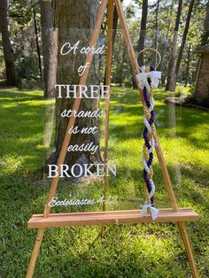 a wooden easel sitting on top of a grass covered field next to a tree